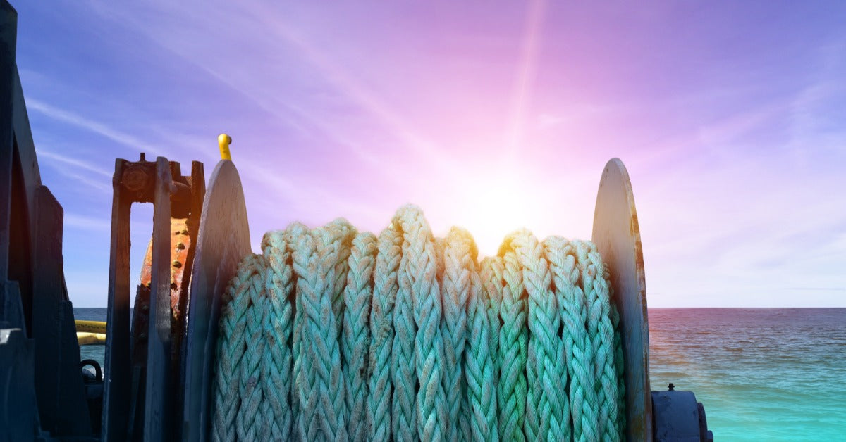 A ship deck mooring winch holding bright blue rope across metal drums, gears, and worn mechanical parts.