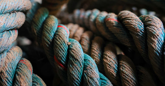 A close-up of thick blue-and-brown twisted rope strands stacked together, showing worn fibers and small red bands.