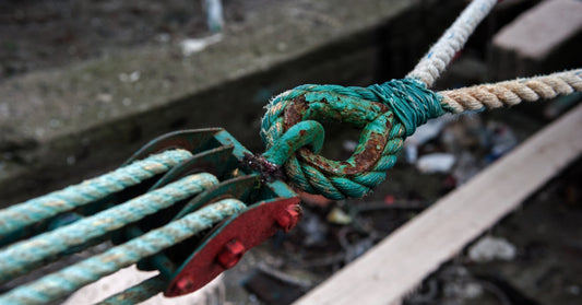 A close-up of a weathered green rope tied through a rusty metal ring with pale ropes stretching across a work area.