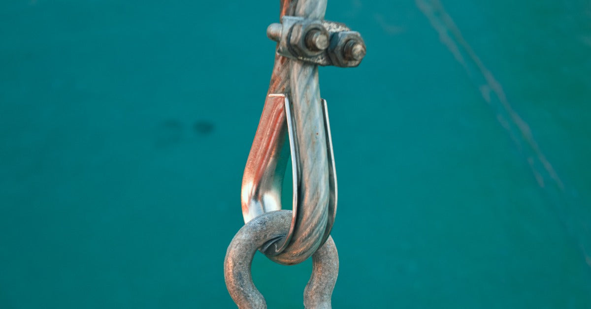 A steel wire rope looped through a metal pulley hook and weathered shackle against a blurred green background.