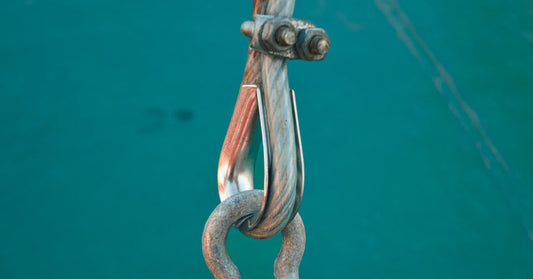 A steel wire rope looped through a metal pulley hook and weathered shackle against a blurred green background.