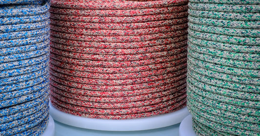 Large coils of braided sailing rope in blue, red, and green patterns arranged side by side on separate white spools.